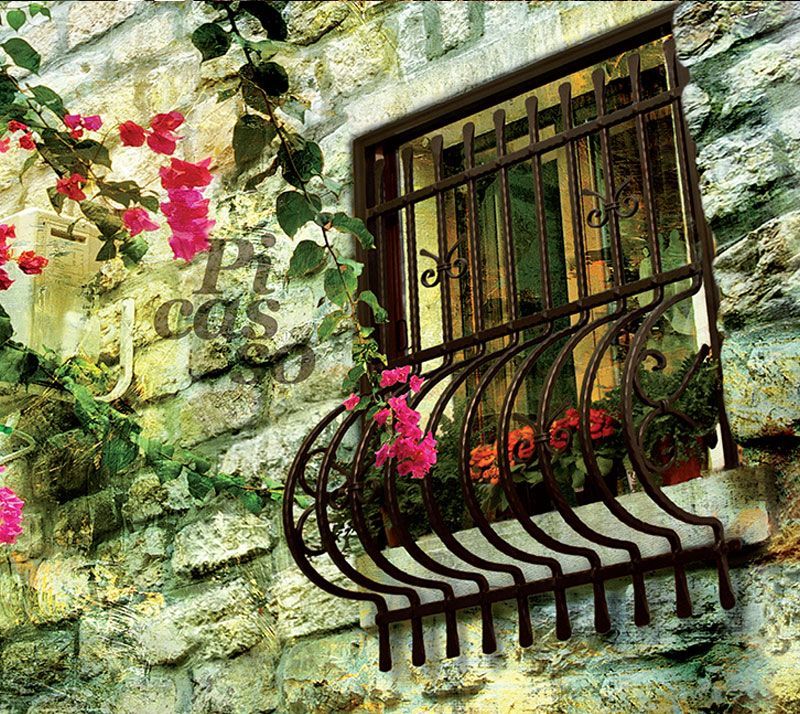 Muro in pietra con finestra sbarrata e fioriera nera, incorniciato da fiori rosa e rampicanti verdi.