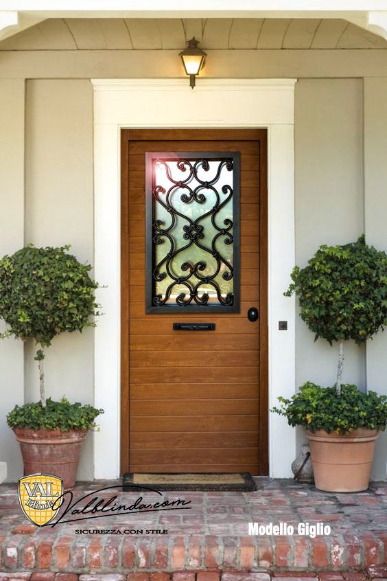 Ingresso principale con porta in legno, pannello decorativo in vetro e piante in vaso su entrambi i lati.