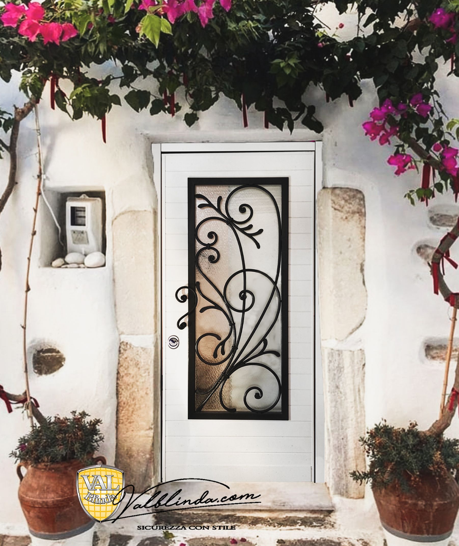 Porta d'ingresso in stucco bianco con anta in vetro e ferro battuto nero, incorniciata da bouganville rosa e piante in vaso.