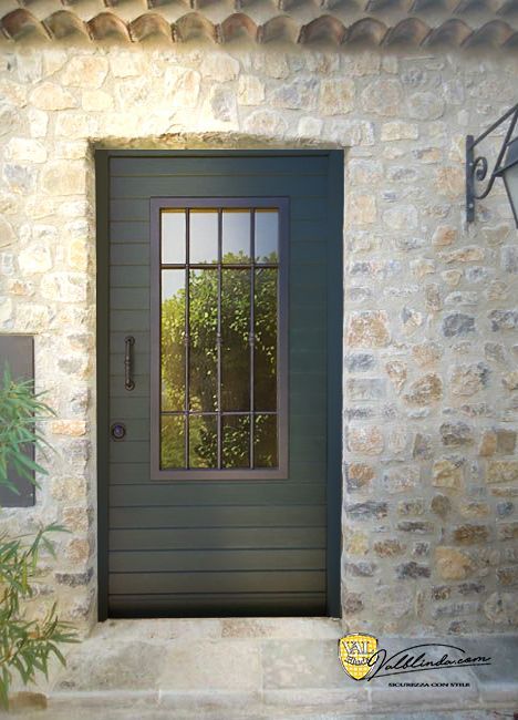 Porta d'ingresso verde scuro con pannello di vetro incastonato in un muro di pietra.