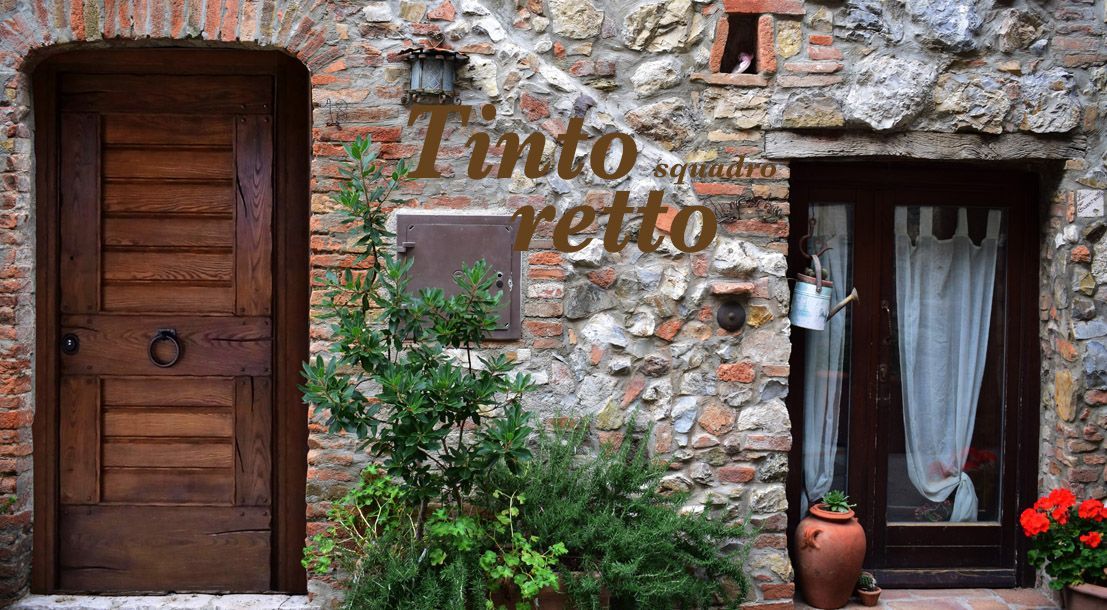 Facciata in pietra con porta in legno, finestra con persiane e piante in vaso davanti a un muro rustico.