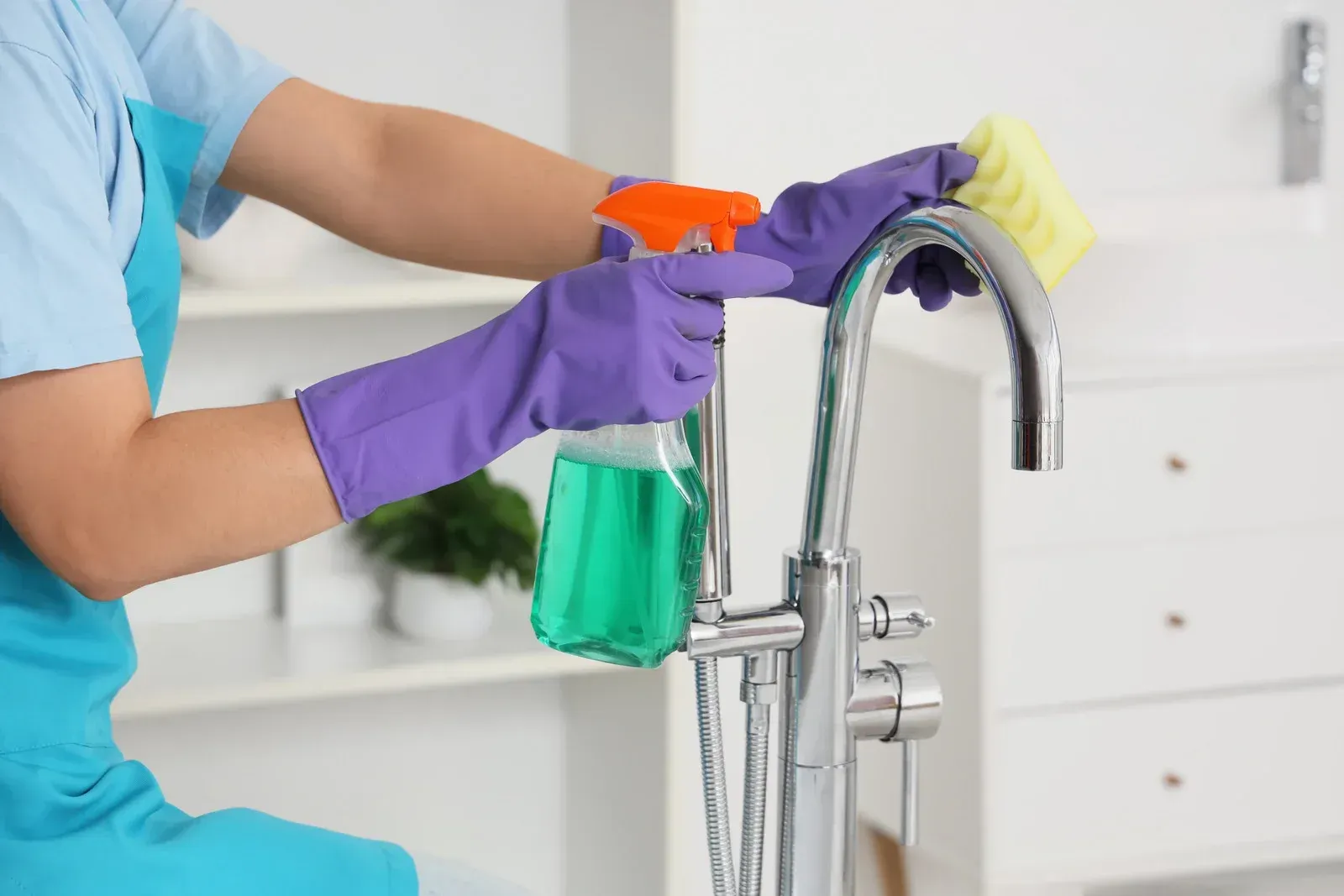 A hand in a yellow rubber glove wipes a white countertop in a tiled bathroom.
