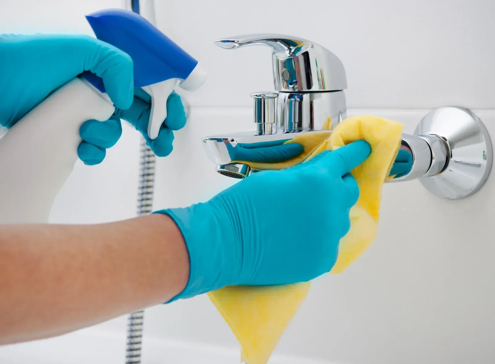A hand in a yellow rubber glove wipes a white countertop in a tiled bathroom.