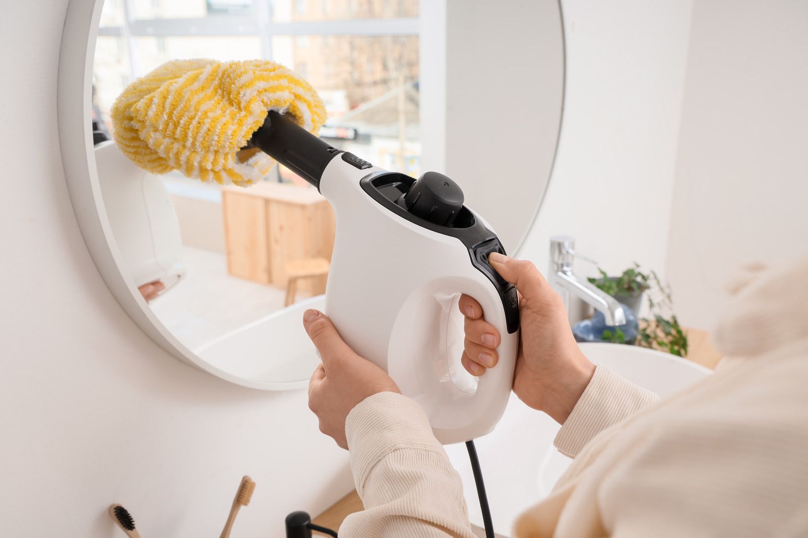 A person wearing yellow rubber gloves wipes a shelf with a blue cloth in a bright, modern room.