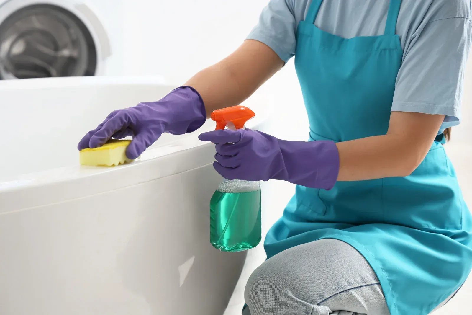 A person wearing yellow rubber gloves wipes a shelf with a blue cloth in a bright, modern room.