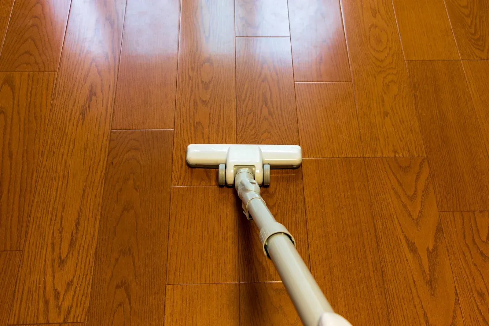 A person in blue work clothes and gloves mops a wooden floor in front of a grey sofa.