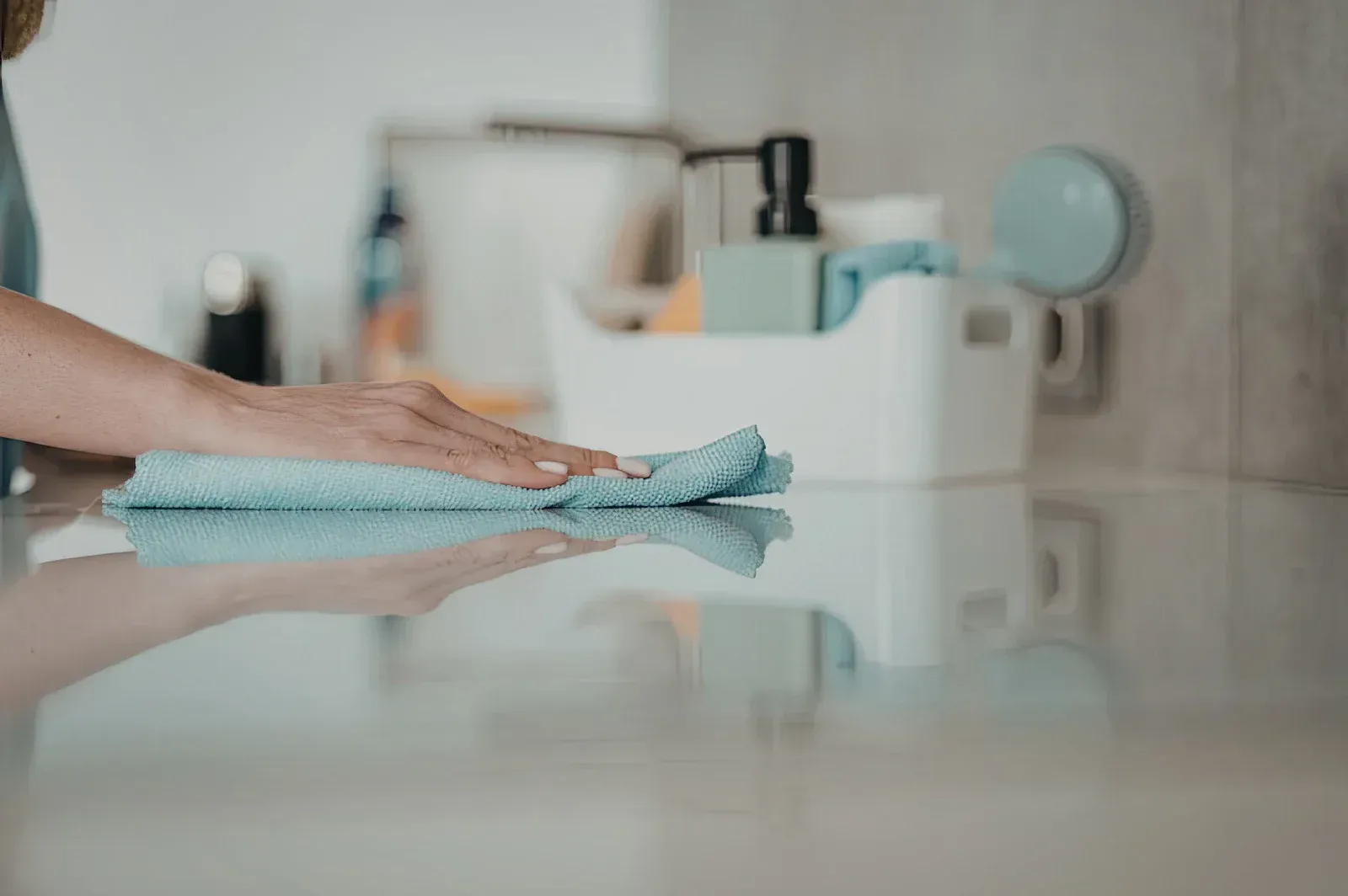 A person in blue work clothes and gloves mops a wooden floor in front of a grey sofa.