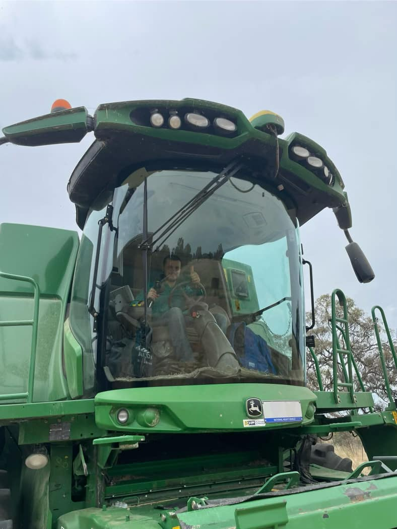 A Man Is Driving A Green Combine Harvester With The Windshield Open — Bendigo Windscreens in Bendigo, VIC