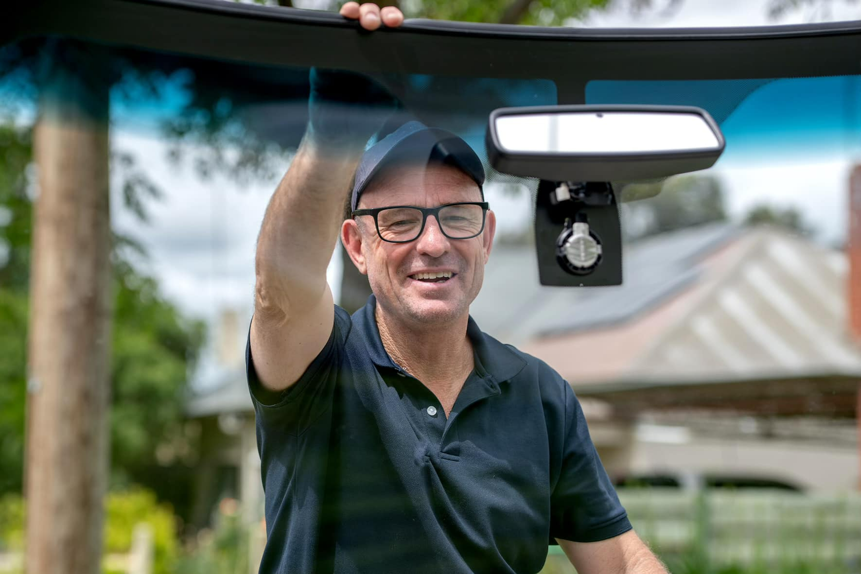 A Man Is Holding The Windshield Of A Car — Bendigo Windscreens in Bendigo, VIC