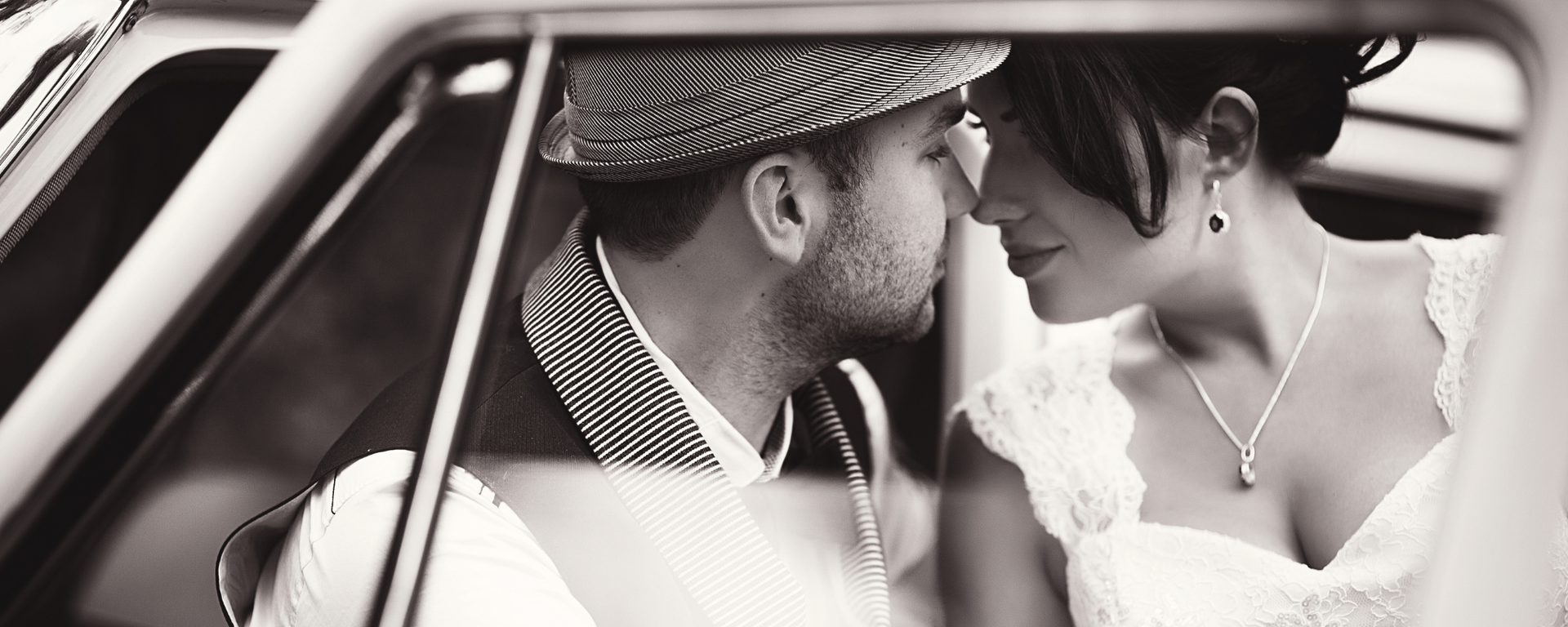 Bride and groom kissing in a car, seen through the window in black and white