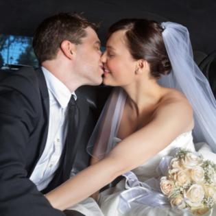 Bride and groom kissing in a car, with a white veil and bouquet visible