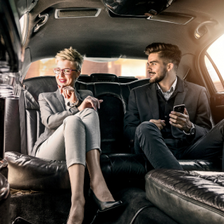 Two people sitting in a black limousine, talking and holding a phone
