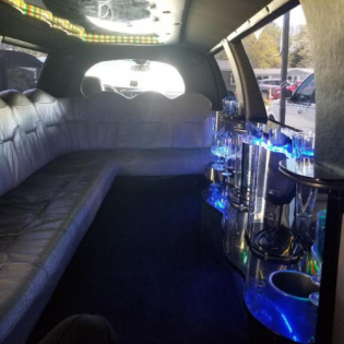 Stretch limousine interior with white leather seats and blue-lit bar shelves.