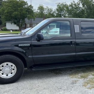 Black Ford Excursion parked outdoors on gravel beside trees and a house