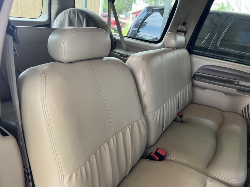 Beige leather car back seat with headrests and seatbelts, viewed from the rear door