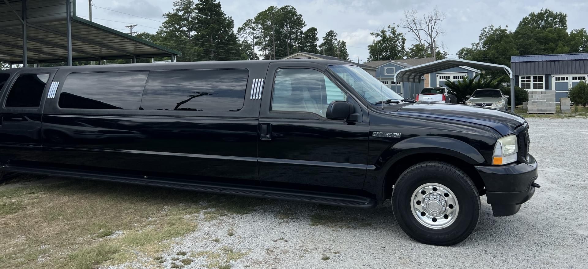 Black stretch limousine parked outdoors on a gravel lot near houses and trees