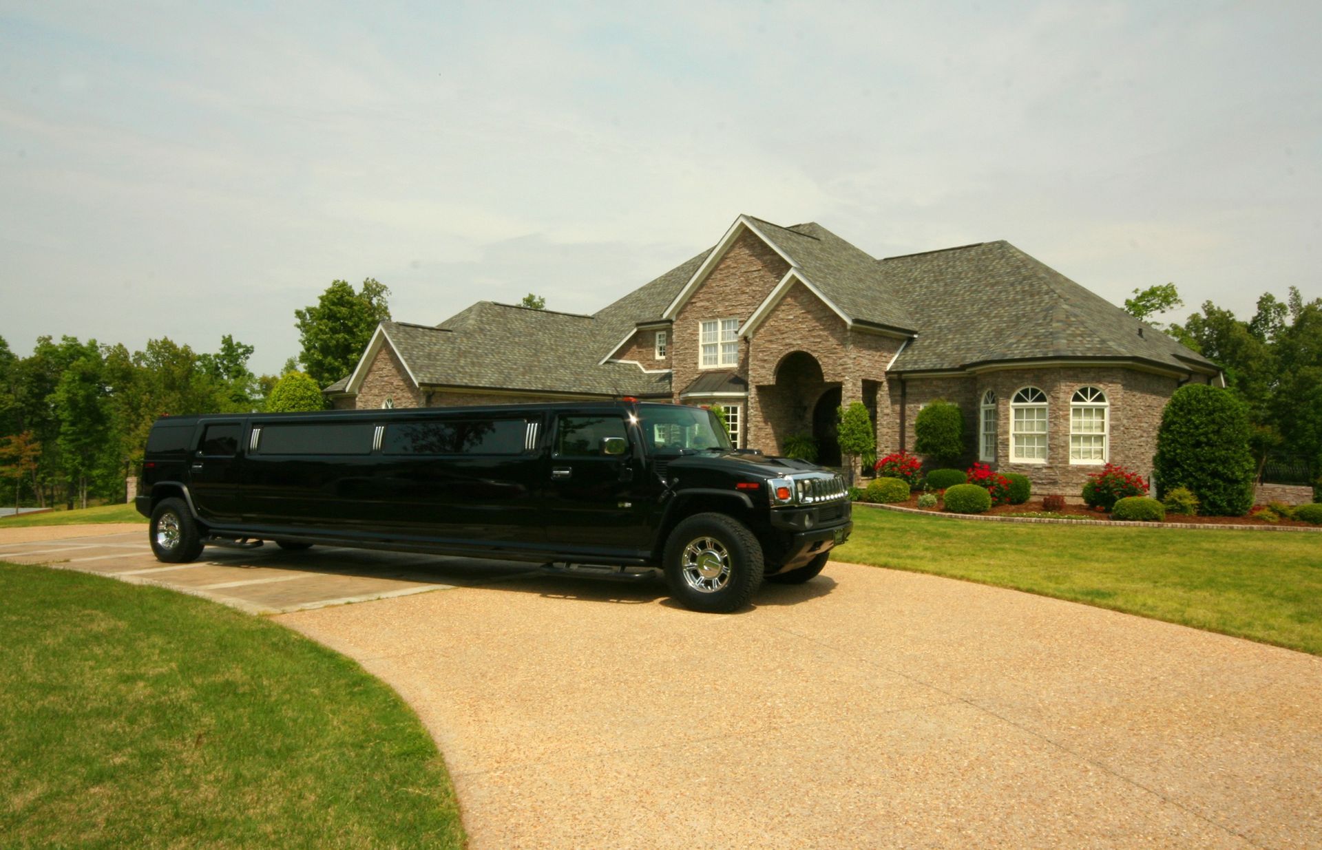 Black stretch limousine parked in a curved driveway in front of a large brick suburban house