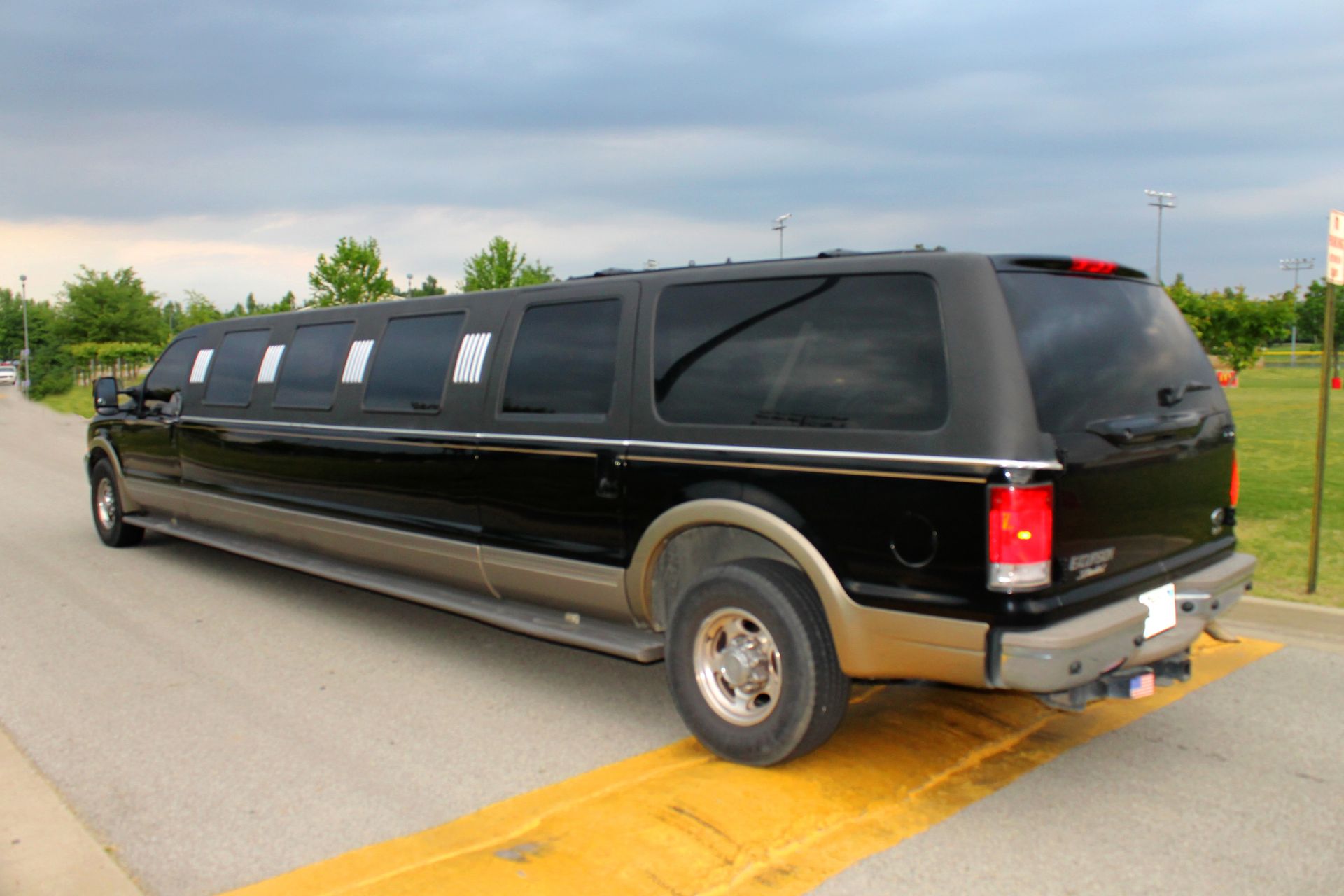 Black stretch SUV limousine on a road, viewed from the rear side.