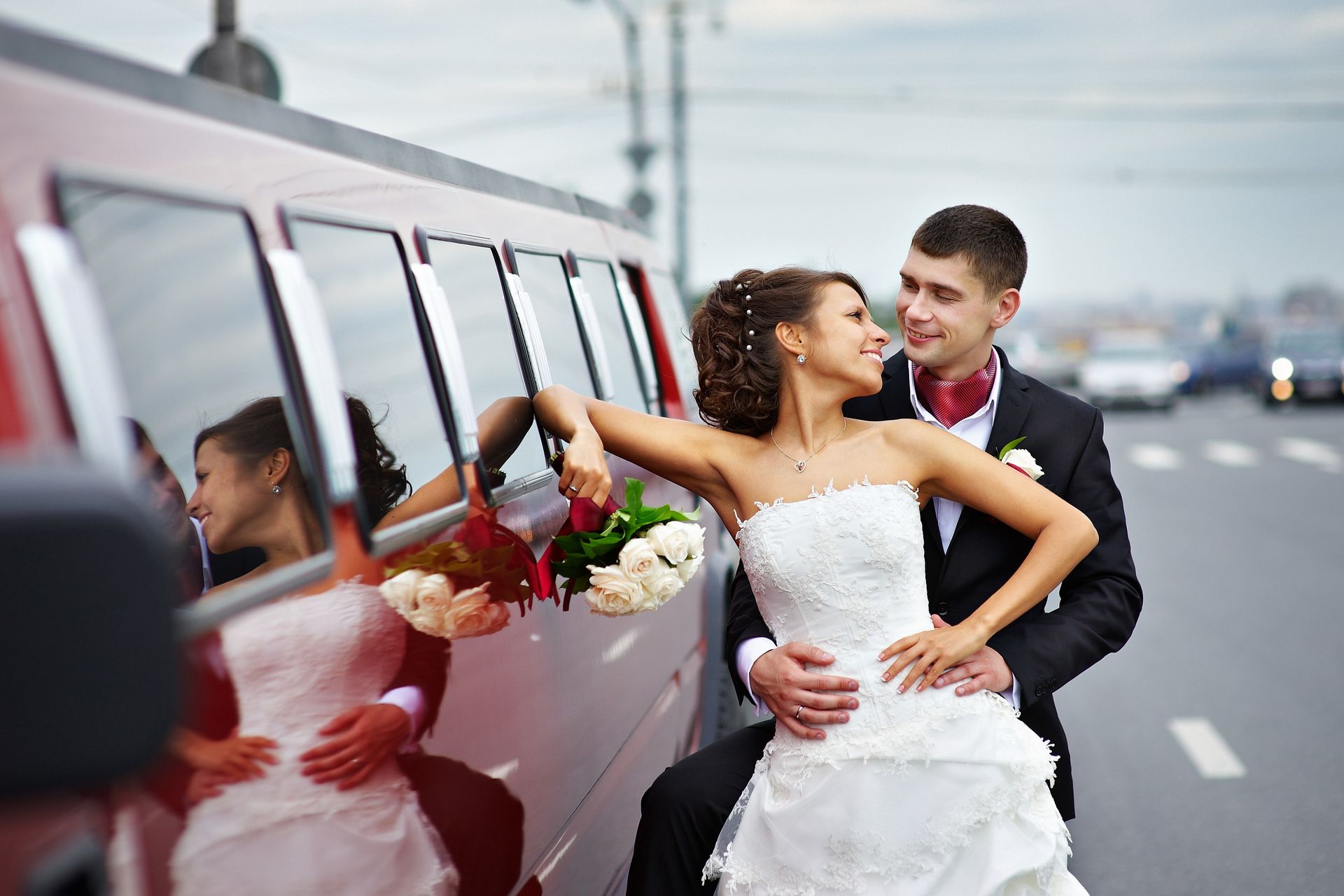 Bride and groom kiss beside a white limousine on a city street