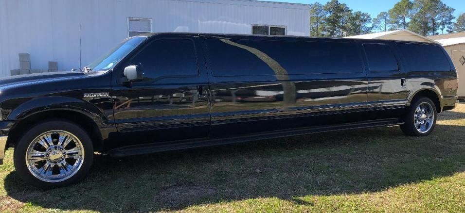 Black stretch limousine parked on grass beside a white building in daylight