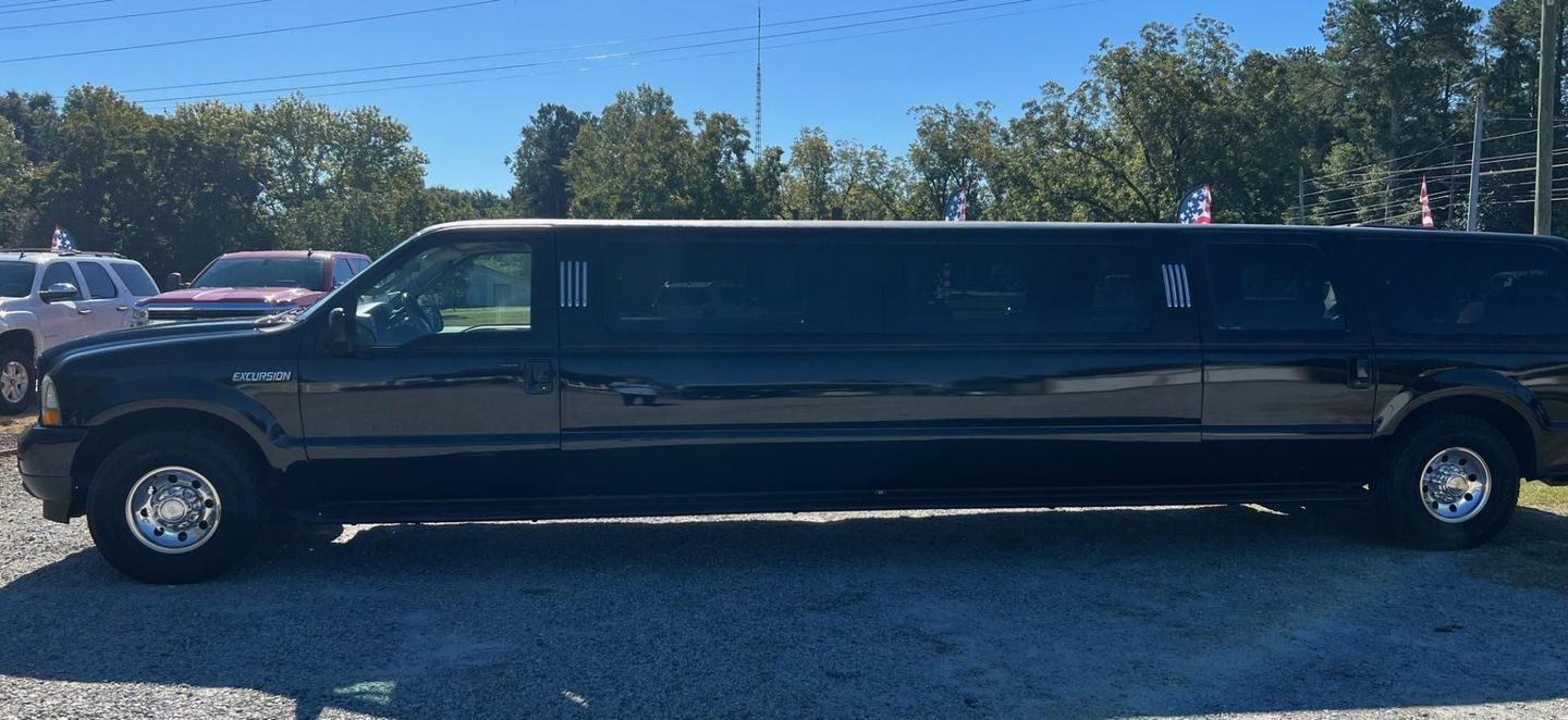 Long black stretch limousine parked in a gravel lot under a blue sky