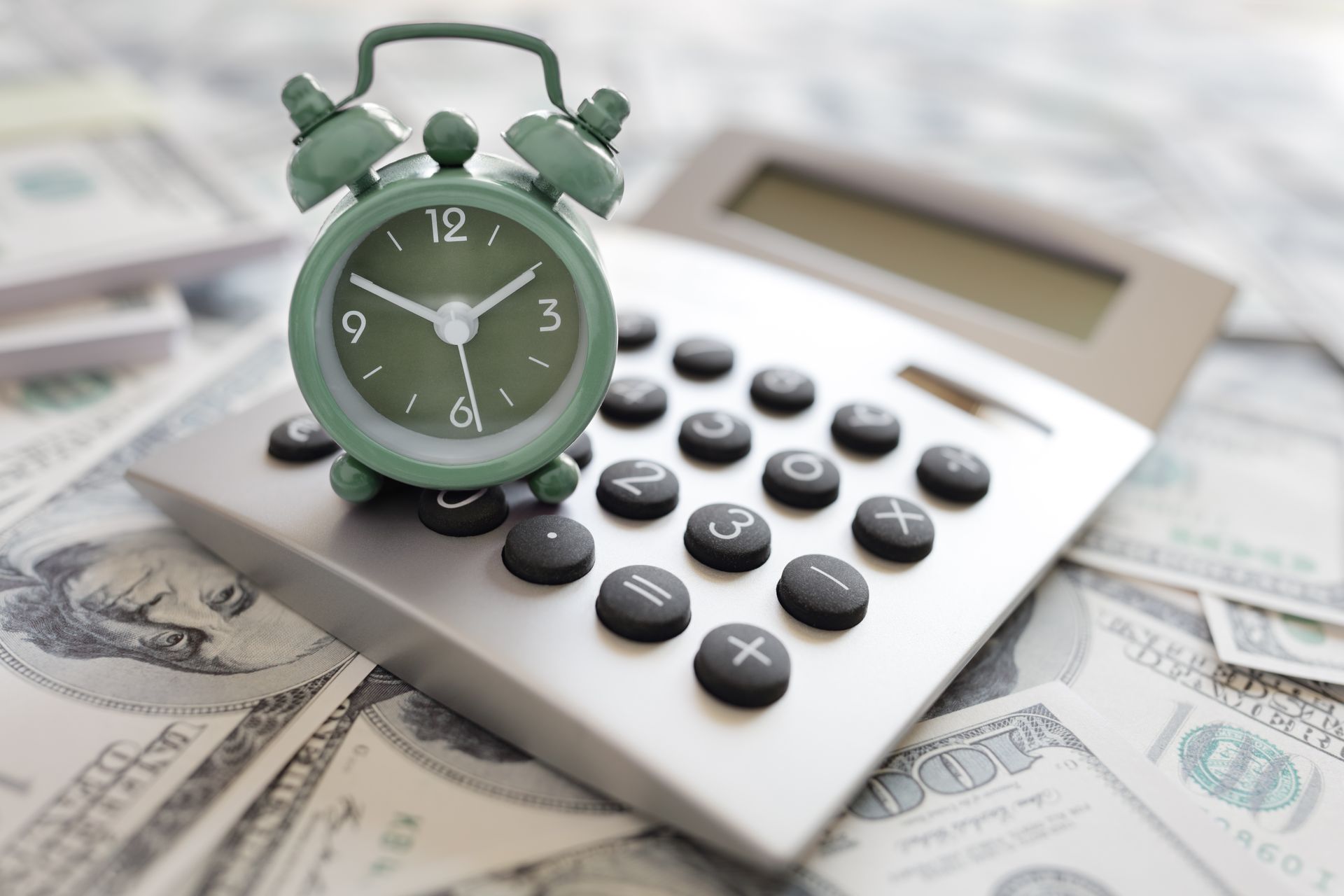 Green clock on a calculator, surrounded by American dollar bills.