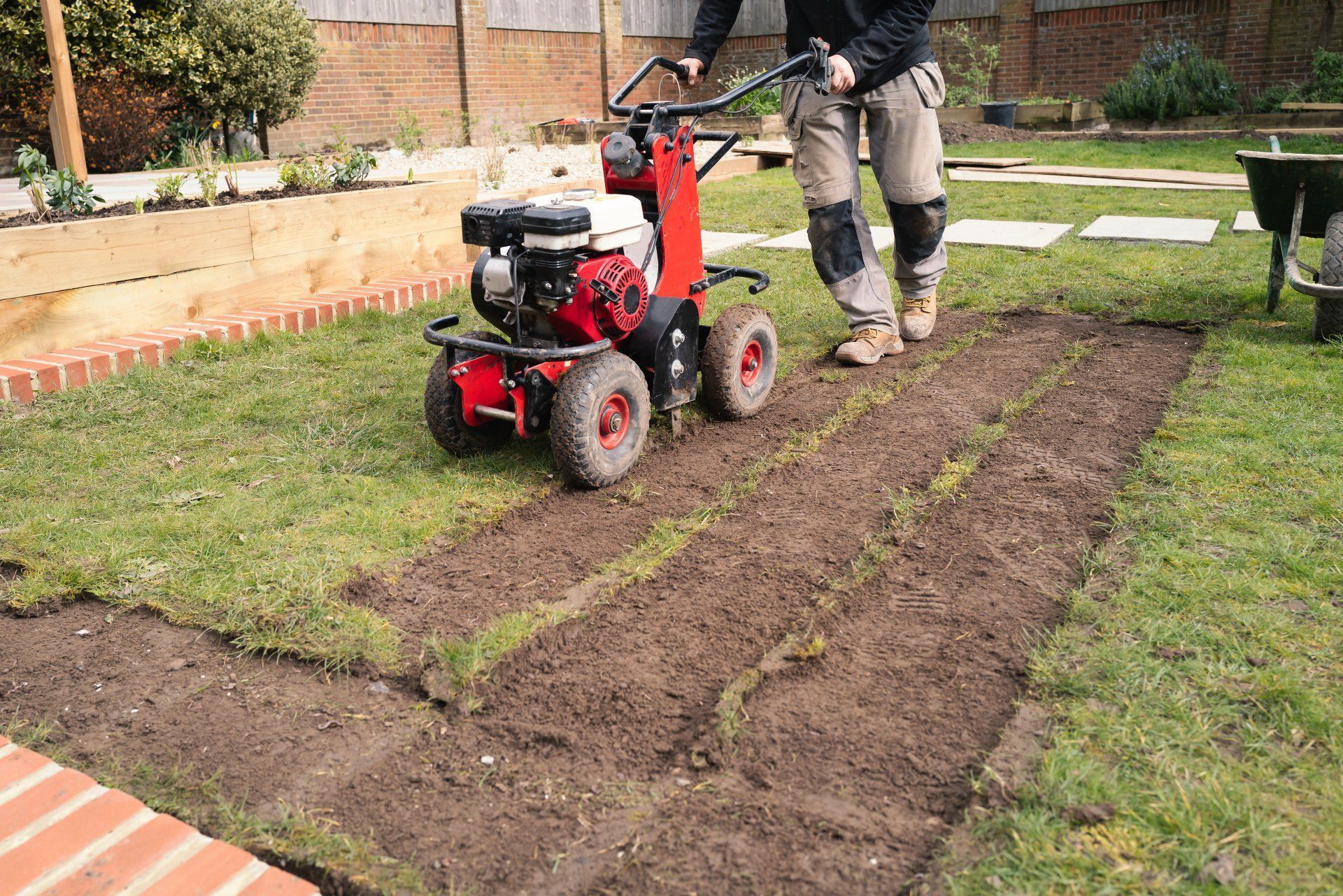 Person using a red tiller to prepare soil in a garden bed