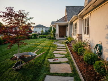 Modern house with landscaped yard, stone path, wheelbarrow, and trimmed lawn at sunset