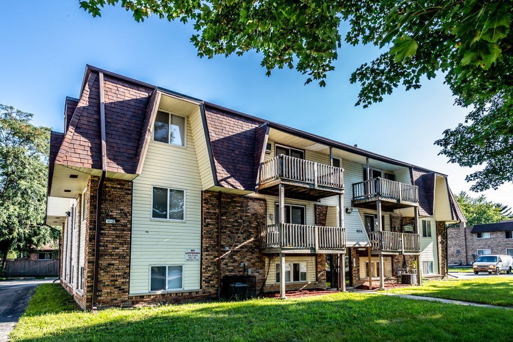 Apartment building with brick and siding, balconies, and brown roof on a sunny day.
