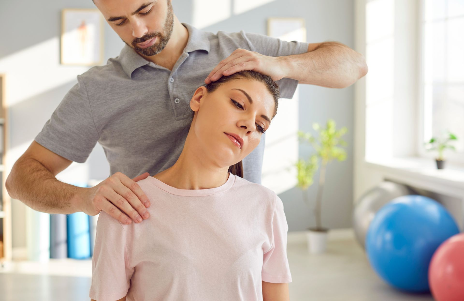 Therapist gently adjusts a woman’s neck in a bright clinic with exercise balls in the background