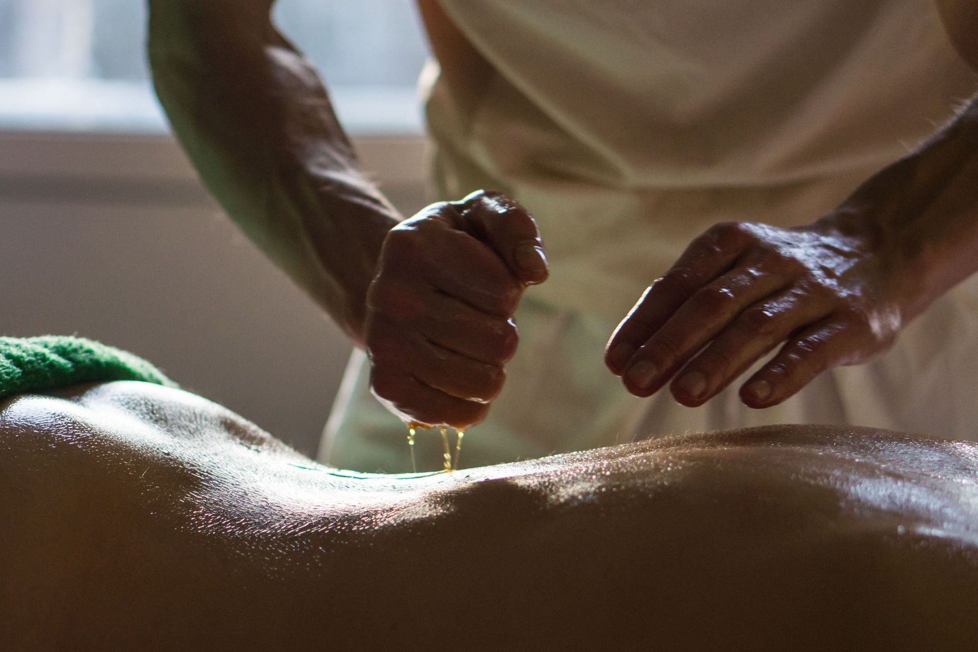 Hands pouring oil onto a person’s back during a massage treatment