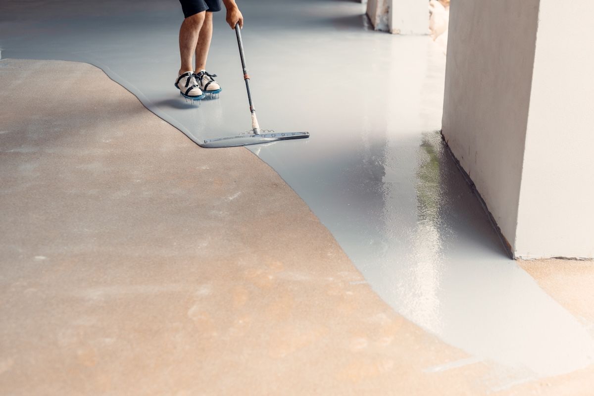 A person applying floor levelling compound. The floor is partially coated in a shiny, wet finish — BLB Flooring Solutions in Newcastle, NSW