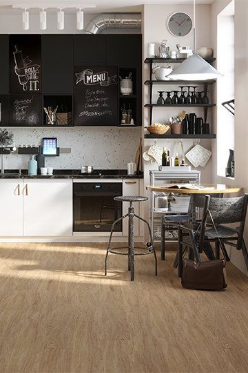 Modern kitchen with white cabinets, black chalkboard wall, and wooden floor. A table and stool are set for dining — BLB Flooring Solutions in Newcastle, NSW