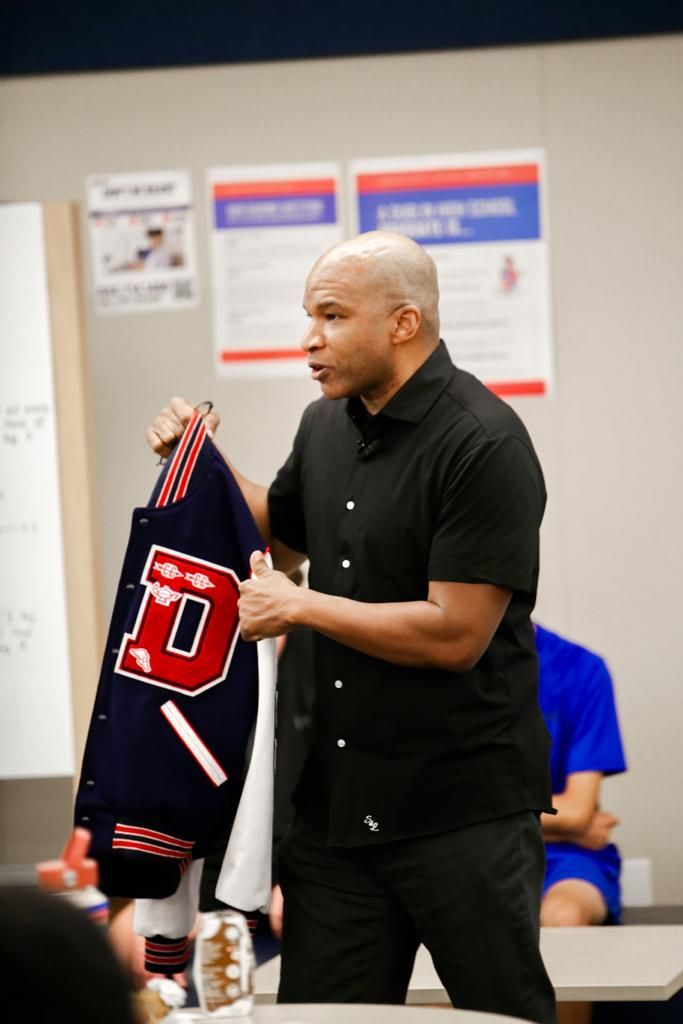Man in black shirt holds letterman jacket with large 