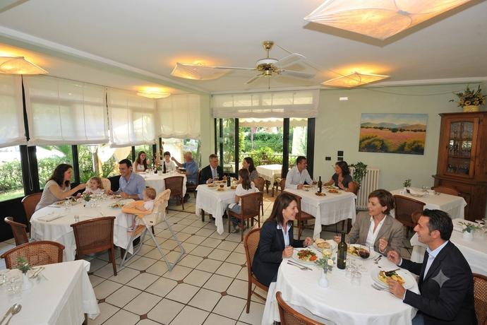 Sala da pranzo vuota di un ristorante con tovaglie bianche, sedie di vimini e grandi finestre con tende.