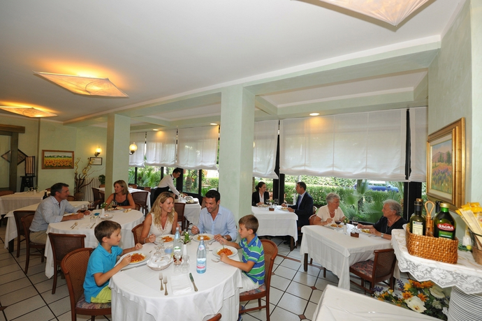 Elegante sala da pranzo con tovaglie bianche, pavimento piastrellato e ampie finestre che si affacciano sul verde.