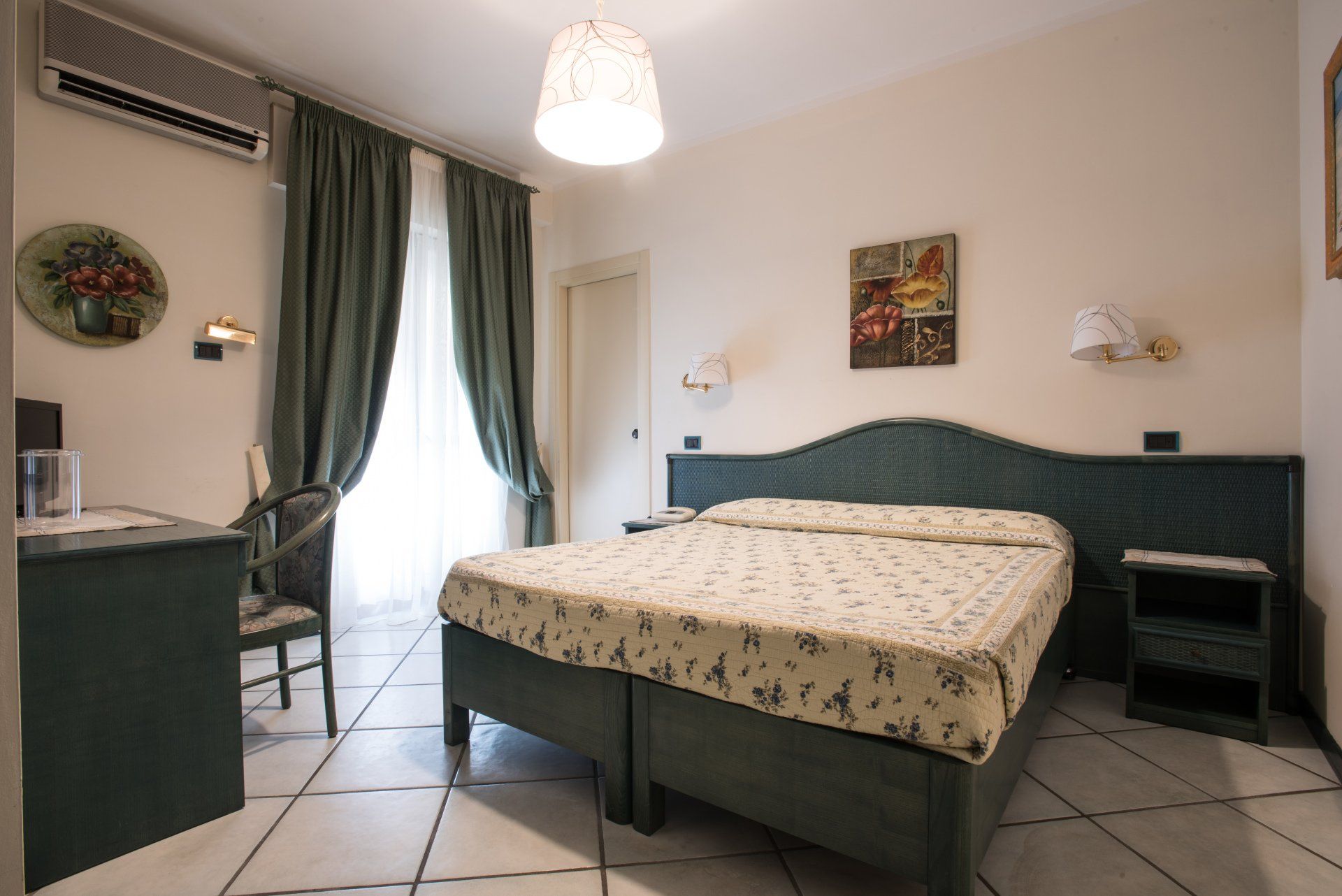 Piccola camera da letto con letto matrimoniale, tende verdi, pavimento piastrellato e scrivania vicino alla finestra.