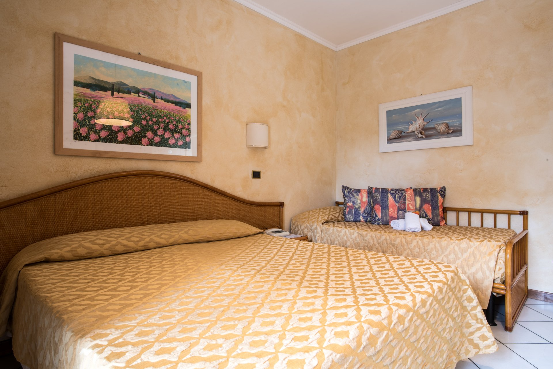 Camera da letto con un grande letto, testiera intrecciata, copriletto giallo a fantasia e quadri appesi alle pareti.