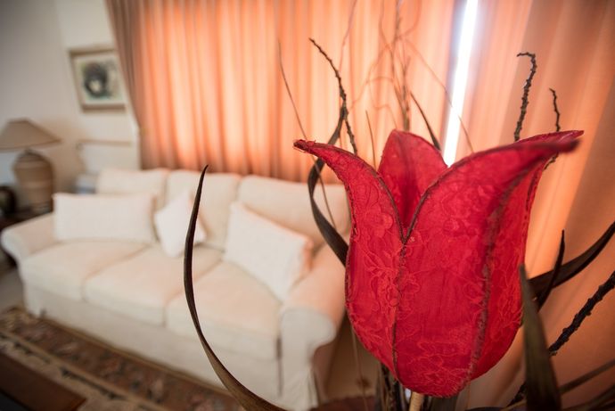 Fiore decorativo rosso in primo piano con divano bianco e tende color pesca in un soggiorno