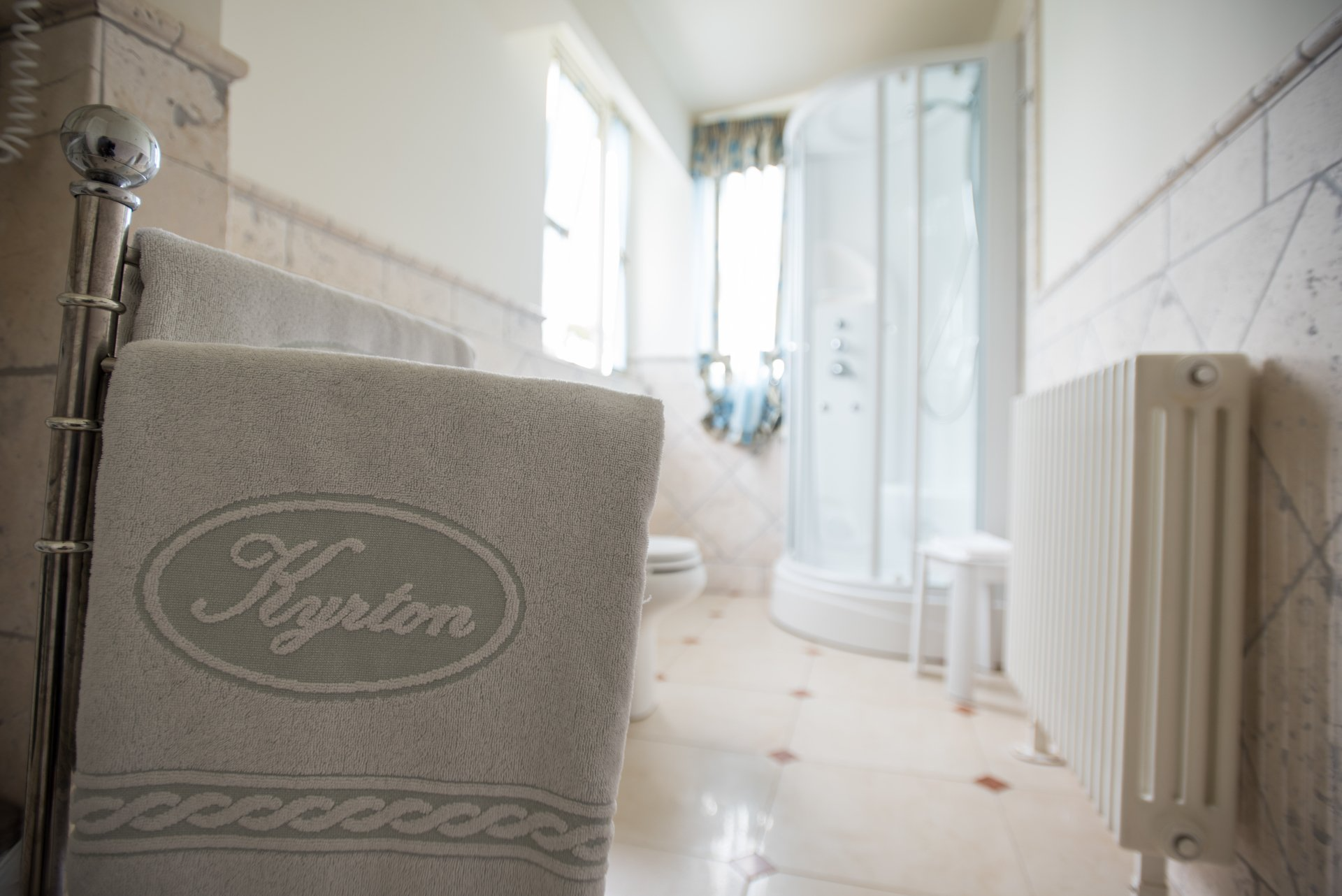 Bagno luminoso con pavimento piastrellato, termosifone e un asciugamano in primo piano vicino alla tenda della doccia.
