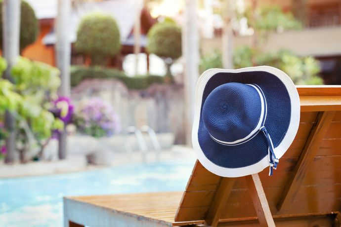Cappello da sole blu su una sdraio di legno a bordo piscina in un soleggiato resort all'aperto.
