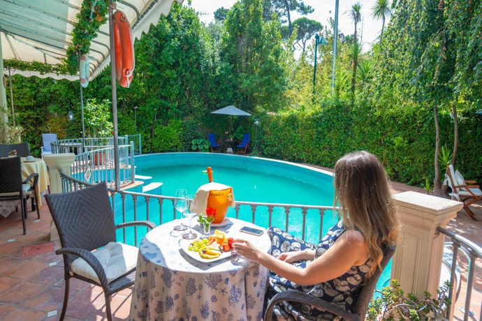 Piscina in giardino con acqua azzurra, ringhiera bianca, sedie da patio e rigogliosi alberi verdi.
