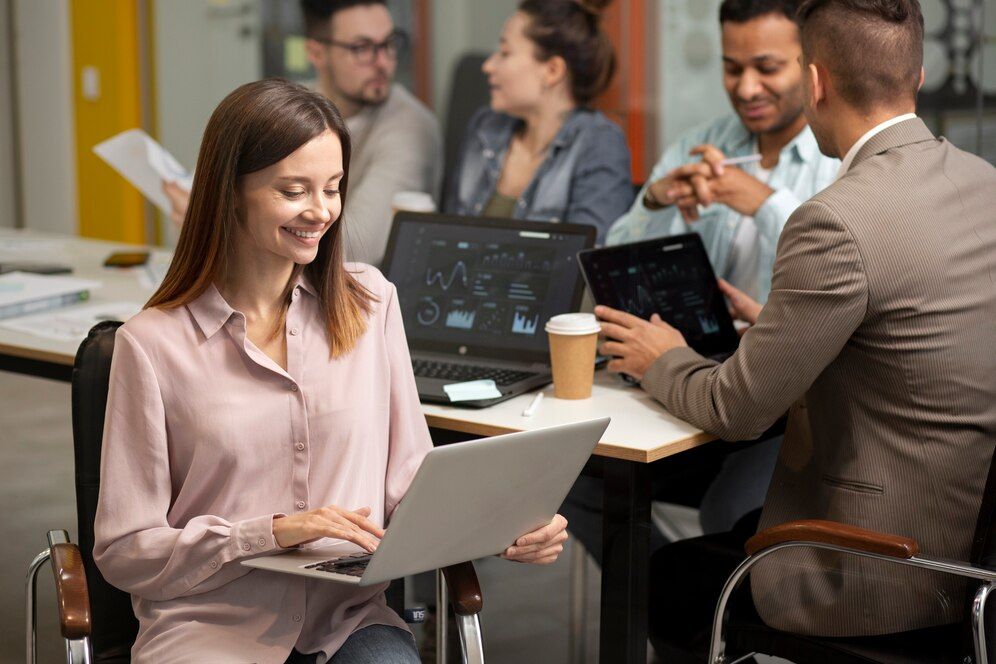 A woman is using a laptop computer while sitting at a table with other people.