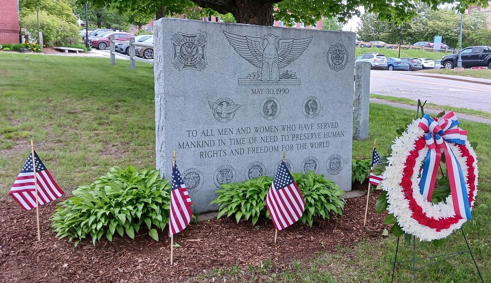 A stone war memorial with American flags and a wreath in front.