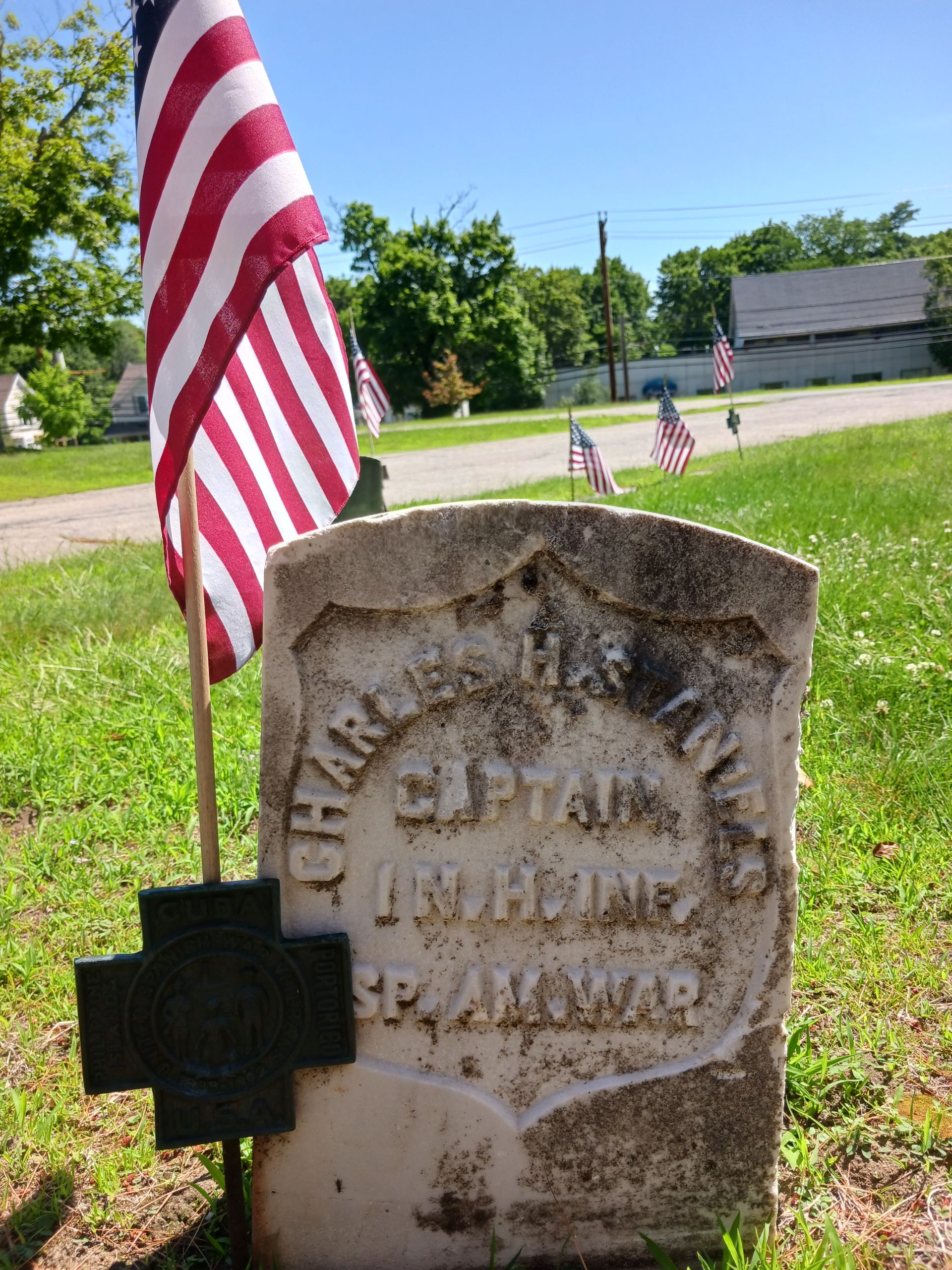 Headstone of Captain Charles H Staniels in a cemetery, with an American flag and cross.