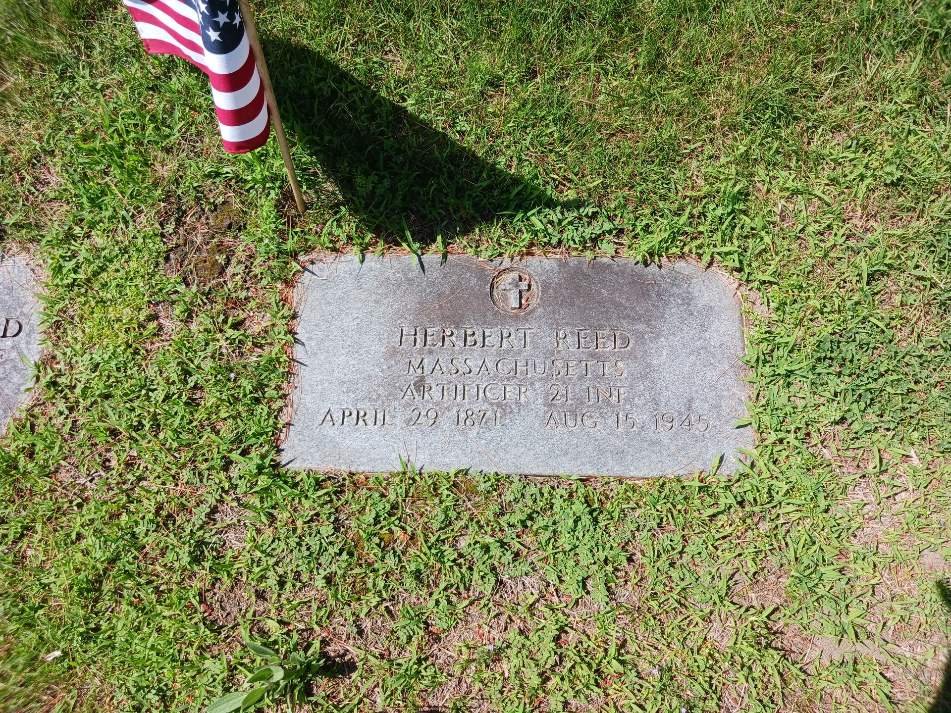 Gravestone in grass with an American flag, reads 