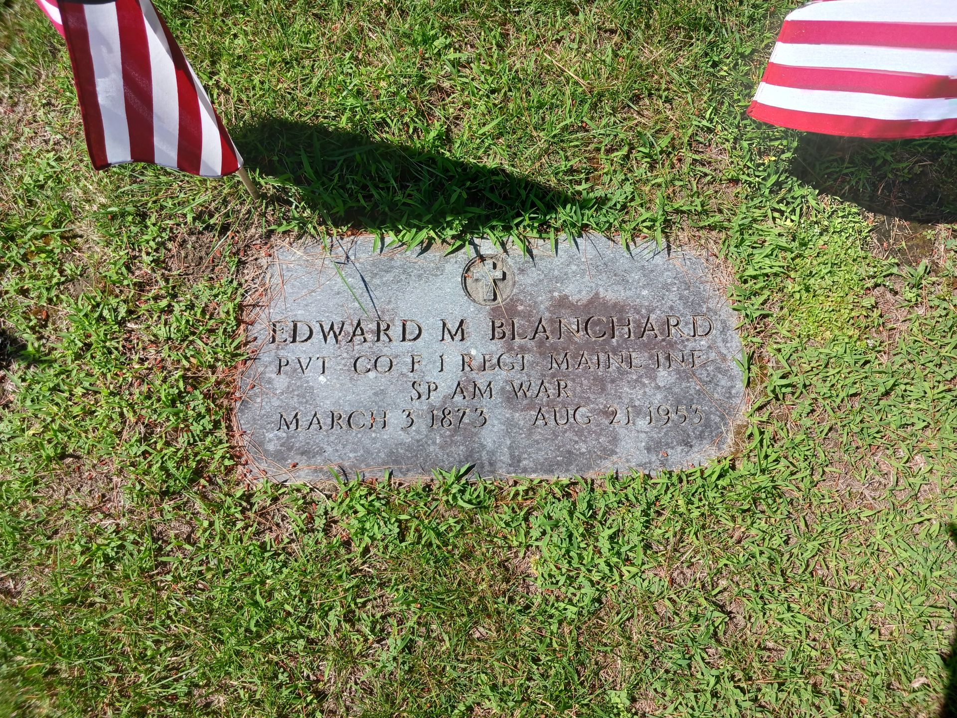 Gravestone of Edward M. Blanchard, a soldier who died in the Spanish American War, with American flags in the background.