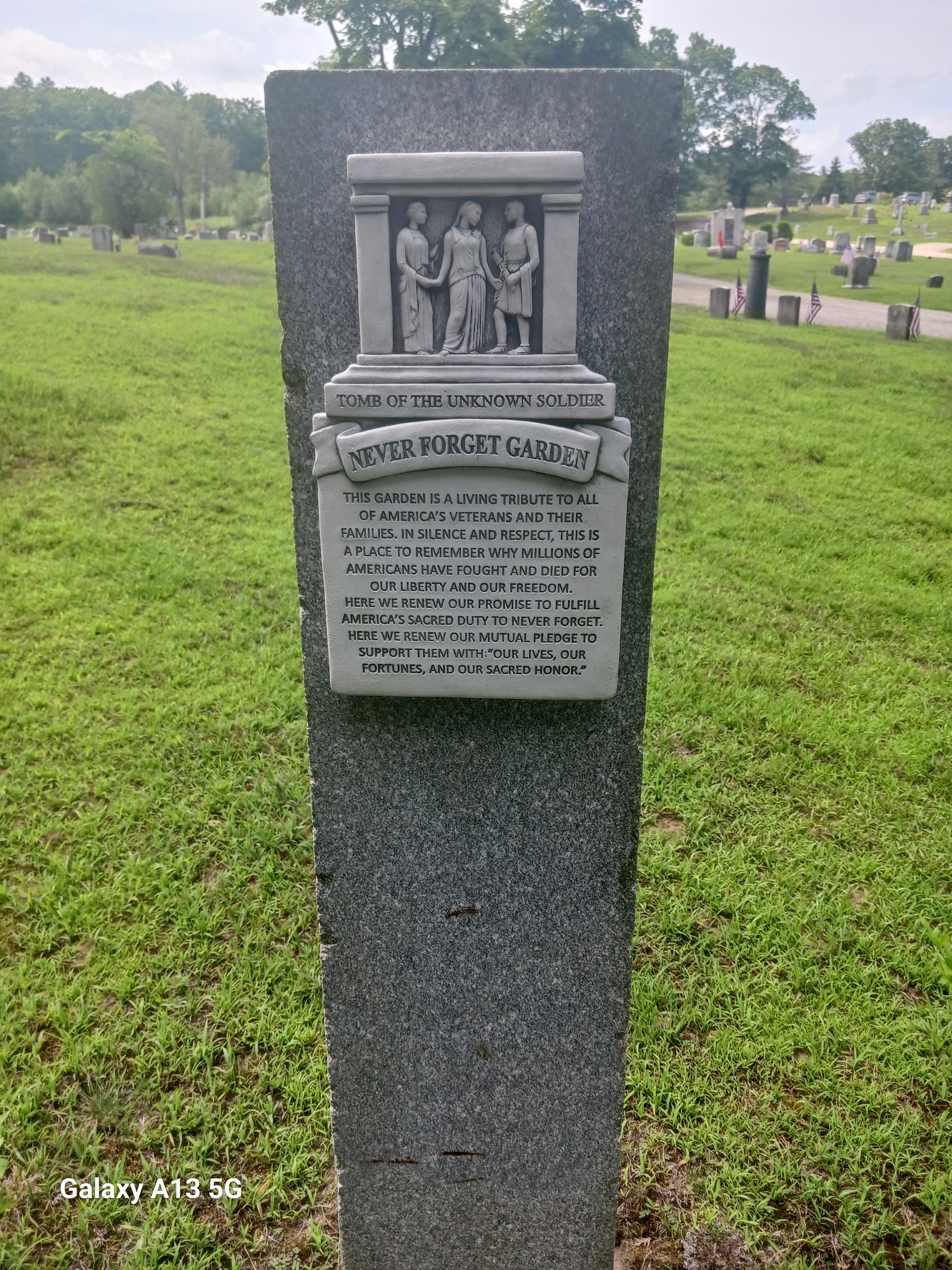 A gray stone monument in a cemetery with a relief of three figures and a plaque that reads 