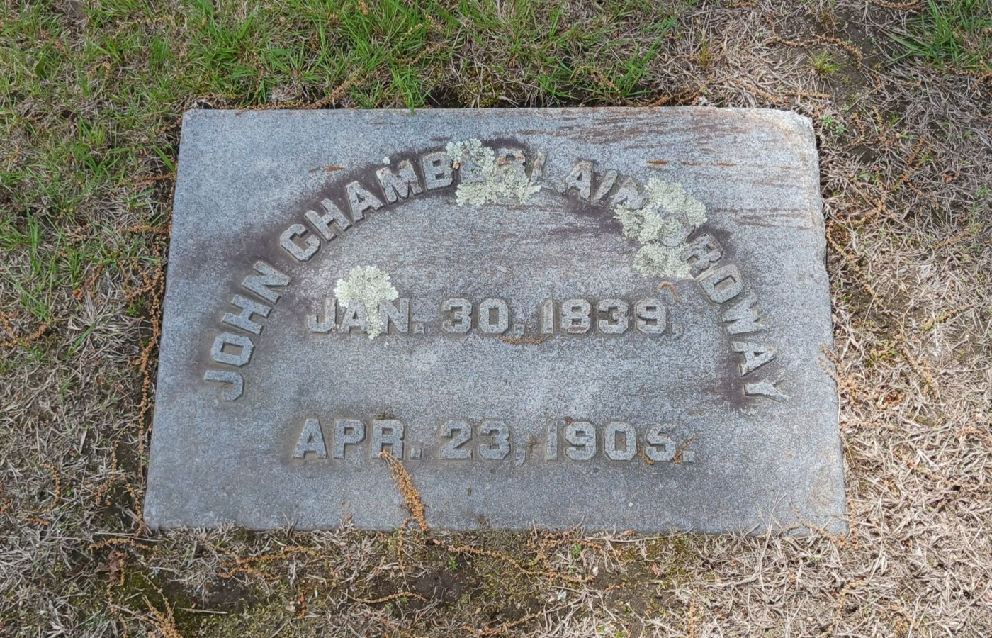 Stained granite footstone with lichen covering raised letters