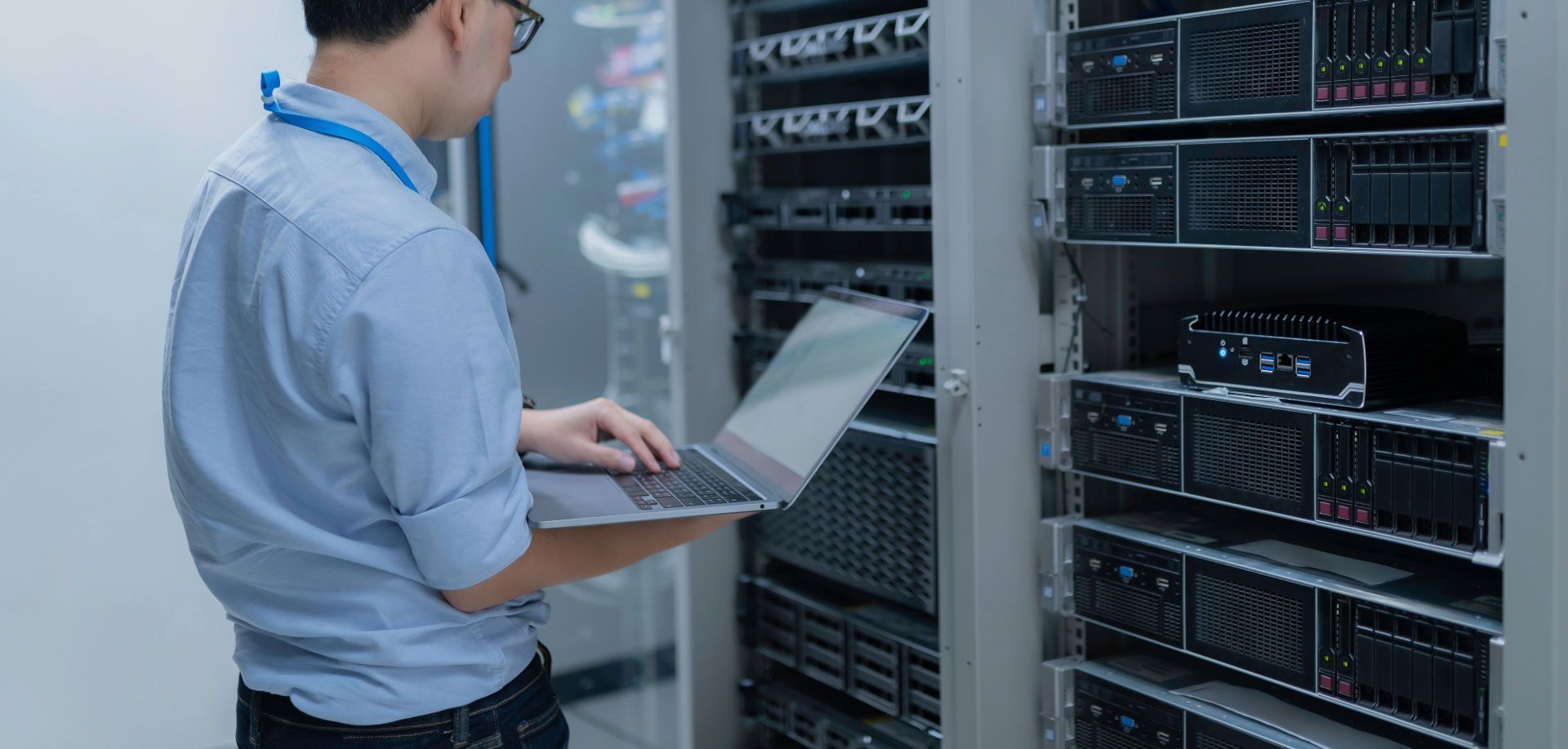Persona con computadora portátil en el centro de datos, inspeccionando los racks de servidores.